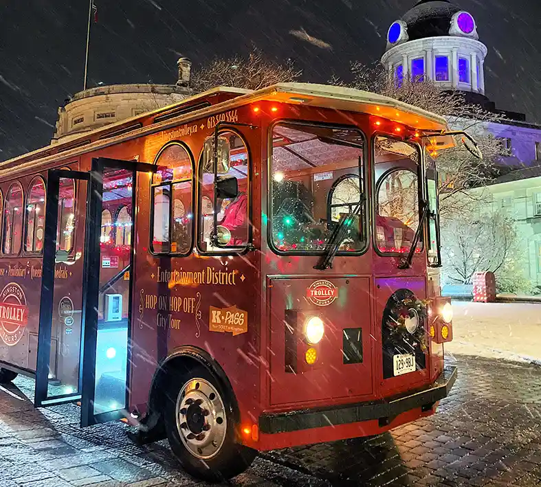 Red Kingston Trolley decorated un christmas lights and garland in a snow storm. Parked outside the front of City Hall. Ready for the Christmas Light Tour