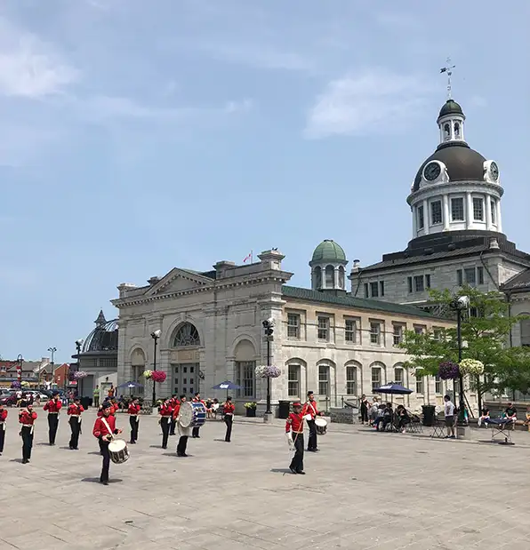 Fort henry guards marching in market square, infront of anj old, grand limestone building